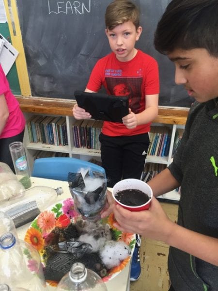 Elementary students building a water filer system with old pop bottles